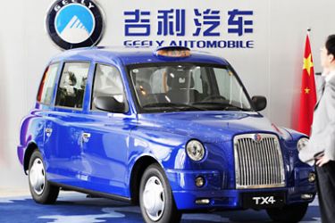 LWU344 - Hangzhou, Zhejiang, CHINA : A Chinese man talks on a mobile in front of a Geely car displayed at the headquater office of China's private automaker