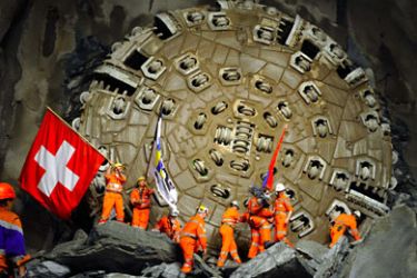 Miners hold national flags stand next to a giant drilling machine that completed the world's longest tunnel beneath the Swiss Alps during a ceremony on October 15, 2010, 30 kilometres (19 miles) from one end and 2,000 metres below the mountains near Sedrun. By the time it opens for