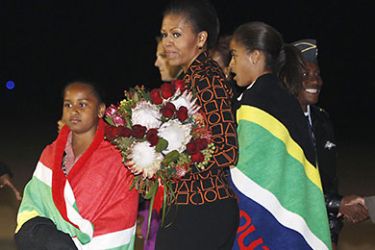 US first lady Michelle Obama holds a bouquet of flowers as daughters Malia(R) and Sasha, are draped in blankets given to them upon landing in Pretoria en route to Johannesburg, South Africa, as they begin their week long trip to Africa on June 20, 2011. AFP