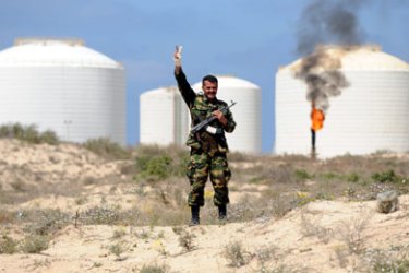 أحد الثوار اللبيين يقف لحراسة ميناء الزويتية أحد موانئ التصدير الرئيسية الخمس في الشرق النفطي، يذكر ان العائدات المالية من تصدير الغاز والنفط كانت في الأوقات العادية تمول 95 في المئة من الموازنة العامة لليبيا. الا ان صناعة النفط الليبية تقع الآن بين مطرقة الأوضاع الأمنية المتدهورة وسندان العقوبات الدولية التي تم فرضها على نظام العقيد معمر القذافي.