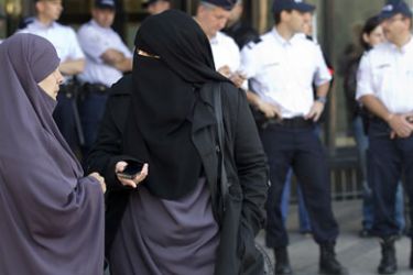 Women wearing niqabs converse as police stand watch in front of the courthouse in Meaux, near Paris, 22 September 2011. The Meaux court, on 22 September, convicted two women for wearing Islamic veils in public - the first conviction since a ban on wearing the veils came into effect in April.