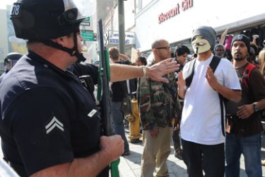 epa03007166 A demonstrator wearing a mask is held back by a Los Angeles police officer during an Occupy LA demonstration in the downtown streets in Los Angeles, California, USA 17 November 2011 on a Day of Action around the nation as authorities close down Occupy encampments. 23 demonstrators were arrested before the march was broken up and the streets cleared.