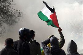Palestinian protester waves his national flag as Israeli tear gas fills the air during a demonstration against Israel's controversial separation barrier in the village of Bilin, near the West Bank city of Ramallah, on December 31, 2010.