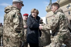 German Chancellor Angela Merkel (C) is shown a flak jacket by German soldiers as she visits Camp Marmal, the German troops' base in Mazar-i-Sharif, on March 12, 2012.