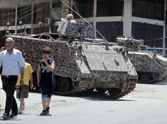 BEI338 - Tripoli, -, LEBANON : People walk past Lebanese army troops deploy in Jabal Mohsen, one of two rival neighbourhoods in the northern Lebanese port city of Tripoli, on May 15, 2012 to order battling gunmen off the streets