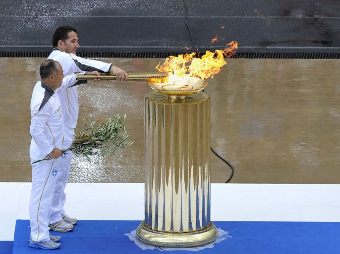 The last torchbearers, olympic gold medalists , Greek weightlifting athlete Pyrros Dimas and Chinese gymnastics athlete, Liu Ning (L) lite the flame during the handover ceremony of the Olympic flame for the 2012 London Olympics at the Panathenaic stadium in Athens on May 17, 2012. AFP PHOTO / LOUISA GOULIAMAKI
