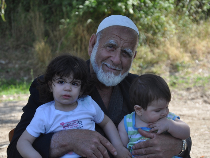 مسن يحمل حفيديه أثناء التواصل مع أرضه بقرية اللجون (الجزيرة نت)