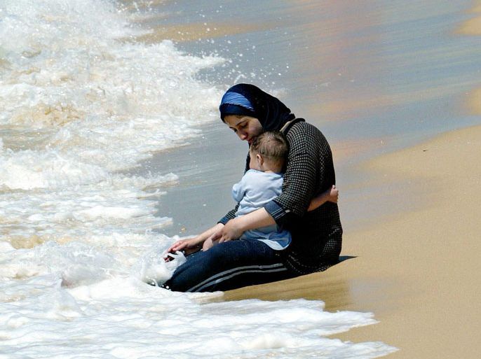 epa000205030 A Palestinan woman holds her baby on a beach at Gaza City in the Gaza Strip on Friday 04 June 2004. EPA/VALDRIN XHEMAJ