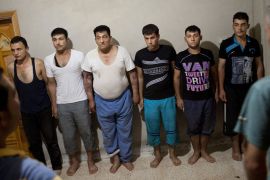 Detainees stand in front of rebels, who say they captured them when they ambushed a military car on the highway from Aleppo to Damascus, at an unknown location the village of Kfar Nubul in Idlib province on July 11, 2012.
