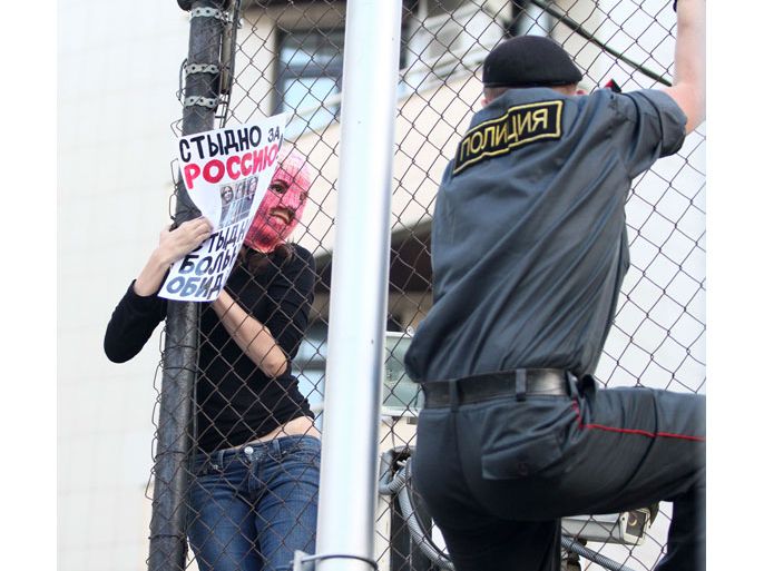 RUSSIAN FEDERATION : A Russian policeman climbs on a fence to get hold of a masked supporter of the all-girl punk band "Pussy Riot" as she holds a poster reading "It's a shame of Russia!" inside the Turkish embassy near the court building in Moscow on August 17, 2012. A Moscow court Friday handed a two-year jail sentence to the three feminist punk rockers who infuriated the Kremlin and captured world attention by ridiculing President Vladimir Putin in Russia's main church. TOPSHOTS/AFP PHOTO / ANDREY BULBASHOV