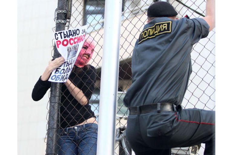 RUSSIAN FEDERATION : A Russian policeman climbs on a fence to get hold of a masked supporter of the all-girl punk band "Pussy Riot" as she holds a poster reading "It's a shame of Russia!" inside the Turkish embassy near the court building in Moscow on August 17, 2012. A Moscow court Friday handed a two-year jail sentence to the three feminist punk rockers who infuriated the Kremlin and captured world attention by ridiculing President Vladimir Putin in Russia's main church. TOPSHOTS/AFP PHOTO / ANDREY BULBASHOV