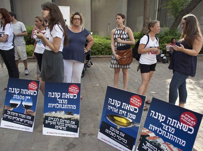 Peace Now activists stand next to posters in Tel Aviv, calling for a boycott of settlement products July 12, 2011. The petition is part of the movement's campaign launched in protest of a new law passed on Monday, under which advocating a boycott of West Bank settlements could lead to financial penalties in Israel. Critics of the bill pushed through parliament by right-wing lawmakers called