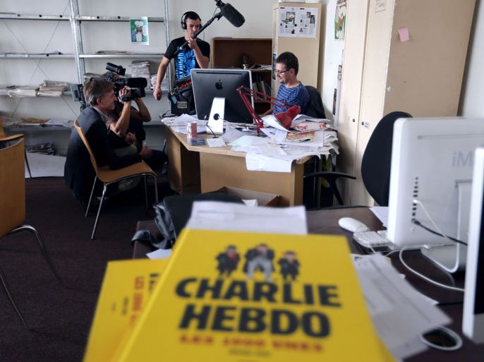 French satirical weekly Charlie Hebdo's publisher and cartoonist, known only as Charb (R), works at his desk on the last issue which features on the front cover a satirical drawing he drew, entitled "Intouchables 2", while journalists are filming an recording, on September 19, 2012 at the weekly's headquarters in Paris. Inside pages contain several cartoons caricaturing the Prophet Mohammed. The magazine's decision to publish the cartoons came against a background of unrest across the Islamic world over a crude US-made film that mocks Mohammed and portrays Muslims as gratuitously violent. The title refers to "Intouchables