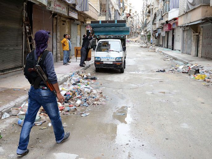 A rebel fighter walks next to Syrian civilians loading their belongings onto a truck at a street strewn with garbage and debris following fighting between Syrian government troops and rebel fighters in the Salaheddin district of the northern Syrian city of Aleppo, on October 25, 2012. The Syrian military and the country's main rebel force have agreed to halt combat operations from Friday morning for the Muslim holiday weekend, but both also reserved the right to respond to attacks