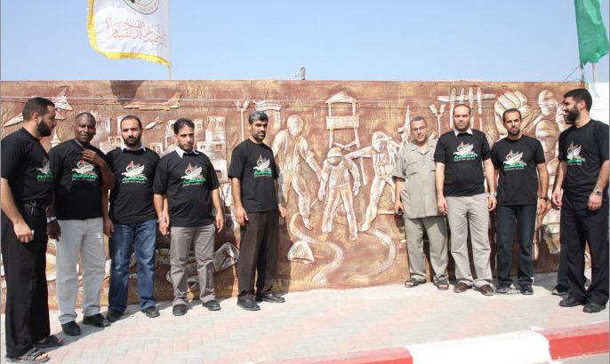 عدد من المحررين بجانب أحد أجزاء الجدارية يظهر فيها عملية اسر شاليط