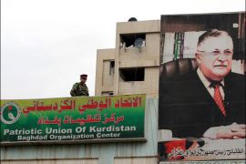 An Iraqi soldier stands guard next to a picture of Iraqi President Jalal Talabani, also leader of the Patriotic Union of Kurdistan (PUK), at the party's headquarters in Baghdad on December 19, 2012. Talabani, a key figure in Iraqi politics for decades who has sought to bridge political and sectarian divides, was showing "improvement" in hospital, a doctor said. AFP PHOTO / SABAH ARAR