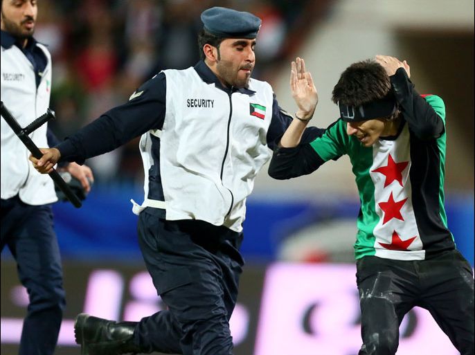 A Kuwaiti policeman arrests a Syrian national (R), sporting the colors of the pre-Baath Syrian flag, after he entered the pitch during his country's game against Jordan at the 7th West Asia Football Federation (WAFF) championship in Kuwait, December 16, 2012. AFP PHOTO/MARWAN NAAMANI