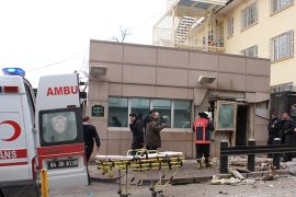People stand outside the entrance of the US embassy in Ankara on February 1, 2013 after a blast killed two security guards and wounded several other people. It was not immediately known what caused the explosion but some media speculated it could have been a suicide bombing. The force of the blast damaged nearby buildings in the Cankaya neighbourhood where many other state institutions and embassies are also located. AFP PHOTO / IHLES NEWS AGENCY