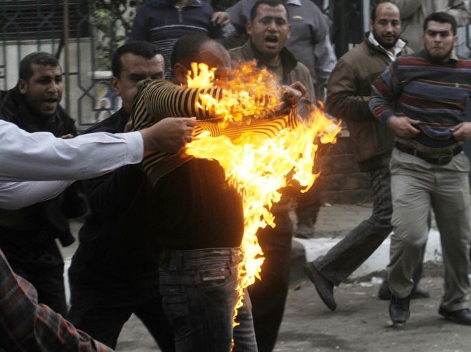 KD89 - Cairo, -, EGYPT : Egyptian members of the Muslim brotherhoods group try to extinguish fire on one of their comrades who he was hit by a molotov cocktail thrown by protesters during clashes in the street that leads to the headquarters of the organization in Cairo on March 22, 2013. Opposition protesters clashed with Islamists near Muslim Brotherhood headquarters in Cairo after activists marched to the building guarded by police and members of Egypt's ruling movement. AFP PHOTO / STR