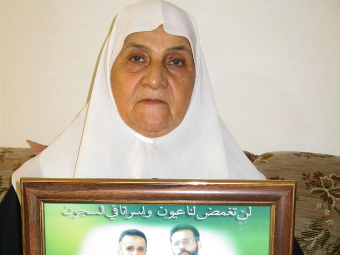 ‪‬ الحاجة أم محمود إغبارية ترفع صورة ابنيها الأسيرين(الجزيرة)