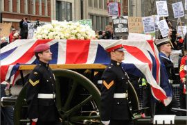 epa03665210 A group of demonstrators wave placards in the background as the gun carriage carrying the Union flag-draped coffin of former British Prime Minister Margaret Thatcher crosses Ludgate Circus, a short distance from St. Paul's Cathedral in central London 17 April 2013 during her ceremonial funeral. Baroness Thatcher died after suffering a stroke at the age of 87 on 08 April 2013. EPA/FACUNDO ARRIZABALAGA