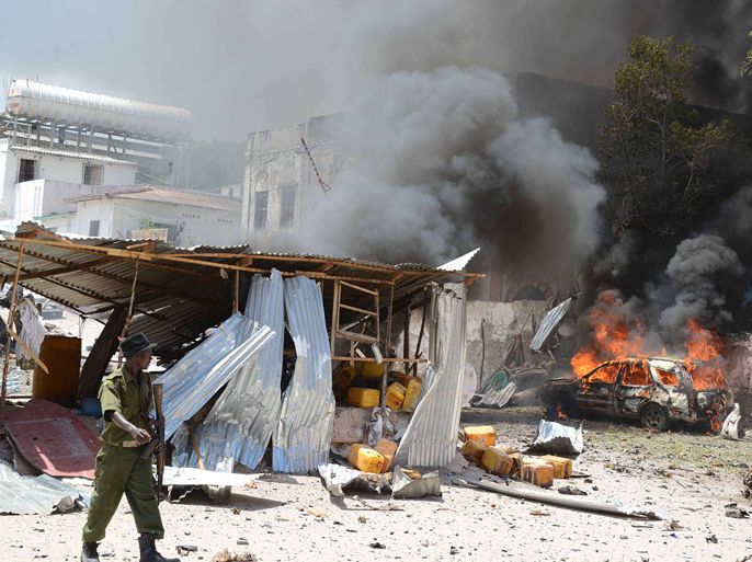 A Somali policeman walks past a burning car on April 14, 2013, in Mogadishu, after a suicide bomber attack in the regional court premises that left several dead. Gunmen wearing suicide vests stormed the main court complex in Mogadishu on April 14, killing at least five people before holing themselves up as Somali and African forces surrounded the building. Several people were wounded minutes later when a remote-detonated car bomb went off as a Turkish aid convoy drove by near the airport, in some of the worst violence to hit Mogadishu in months. AFP PHOTO / MOHAMED ABDIWAHAB