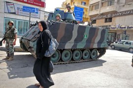 Tripoli, -, LEBANON : A woman walks past Lebanese soldiers standing guard with an armoured personnel carrier (APC) in the northern Lebanese city of Tripoli on May 20, 2013 following running gun battles the previous day between pro- and anti- Syrian government supporters. Violence broke out between members of the largely Sunni city and a small community of Alawites, an offshoot of Shite Islam to which Syrian President Bashar al-Assad belongs, as Syrian troops launched an assault against the rebel stronghold of Qusayr, in Syria's central province of Homs. AFP PHOTO / IBRAHIM CHALHOUB