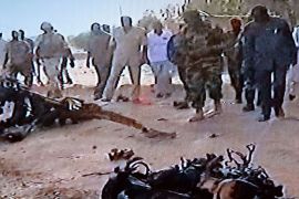 This video grab taken from Niger's TV public channel Tele Sahel on May 23, 2013 shows people standing in front of wreckage of the suicide bomber's motor vehicle, at the Agadez army base, northern Niger, following car bombings in Niger in which at least 20 people died. Islamists groups have claimed responsibility for twin suicide car bombings on an army base and a French-run uranium mine in Niger, in retaliation for the country's military involvement in neighbouring Mali. AFP PHOTO/TELE SAHEL