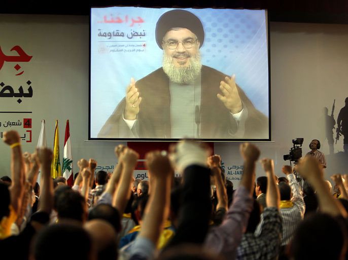Supporters of Hassan Nasrallah (portrait), the head of Lebanon's militant Shiite Muslim movement Hezbollah raise their fists as they watch him giving a televised address in Beirut on June 14, 2013