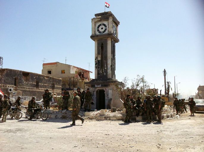 Syrian army soldiers gather in front of a badly damaged clock tower on top of which flies a Syrian flag on the main square of the city of Qusayr on June 5, 2013 in Syria's central Homs province, after the army seized total control of the city and the surrounding region. The Syrian army ousted rebels from the strategic town of Qusayr after a blistering 17-day assault led by Hezbollah fighters, scoring a major battlefield success in a war that has killed at least 94,000 people