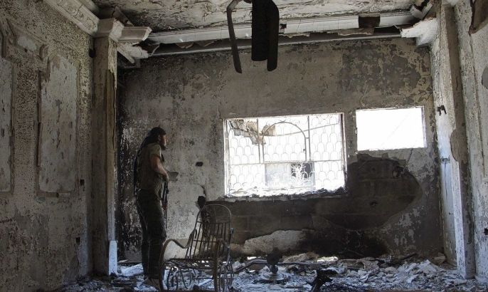 A Free Syrian Army fighter carries his weapon as he looks through a window from a burnt house in Deir al-Zor July 14, 2013. Picture taken July 14, 2013.