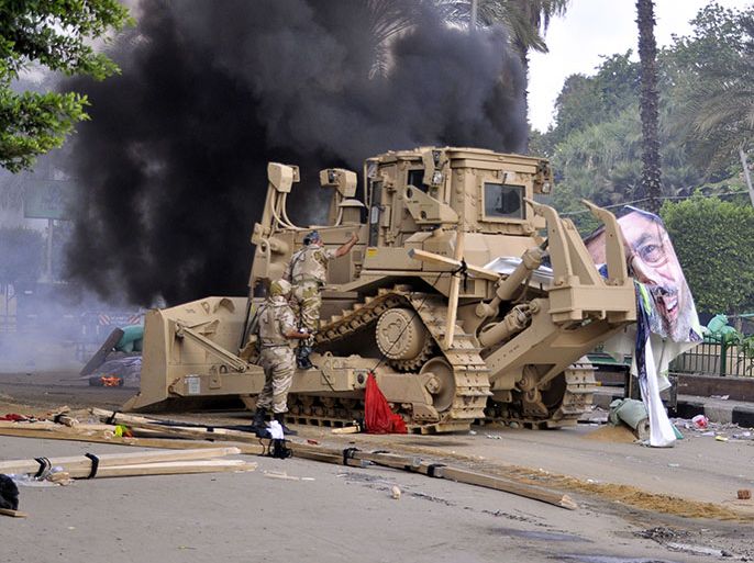 An Egyptian military bulldozer moves in as smoke billows from a burning tent in Cairo's Al-Nahda square after Egyptian security forces dispersed supporters of Egypt's ousted president Mohamed Morsi (portrait) in two huge protest camps in the Egyptian capital by force on August 14, 2013. The operation began shortly after dawn when security forces surrounded the sprawling Rabaa al-Adawiya camp in east Cairo and a similar one at Al-Nahda square, in the centre of the capital.