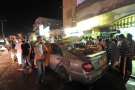 People look at a damaged car belonging to Fawzy Aujali, a colonel with the Libyan army, after a bomb attack in Benghazi, August 3, 2013. Aujali sustained serious injuries to his feet and was rushed to hospital.