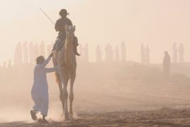 A camel and jockey ride past the finish line as heavy dust is seen during a camel race, an annual event organised for desert dwellers, in the desert of Aleghan, north of Saudi Arabia, in Tabuk June 18, 2013.