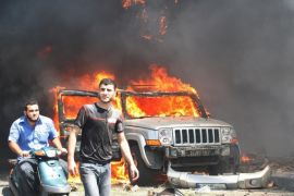 Civilians are seen near a burning car outside one of two mosques hit by explosions in Lebanon's northern city of Tripoli, August 23, 2013. The death toll from twin blasts that hit two mosques in Lebanon's northern city of Tripoli on Friday has gone up to 27, the health minister said.