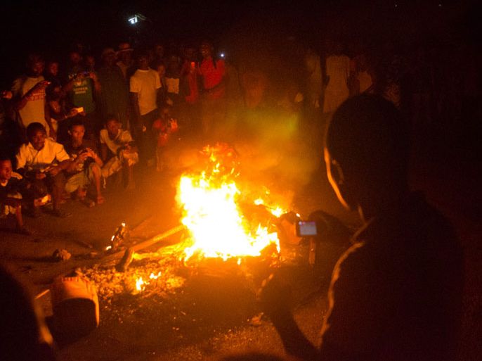 Nosy-Be, -, MADAGASCAR : People take pictures of the body of a Malagasy burning after he was dragged from a vehicle and his body thrown onto a fire on October 3, 2013 in Nosy Be on suspicion of murdering a young boy for his organs. Two European men were lynched hours earlier as the residents of the island went on a day-long rampage after a missing eight-year-old was reportedly found dead. AFP PHOTO BILAL TARABEY