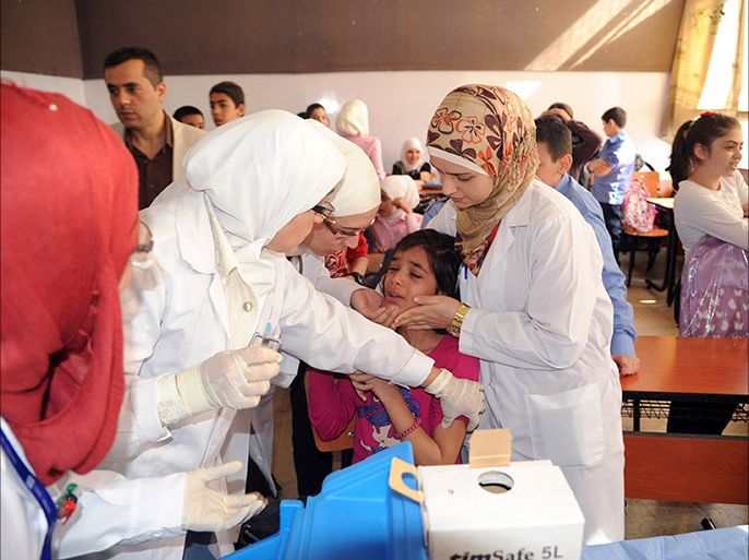 Syrian health workers administer polio vaccination to a girl at a school in Damascus, in this file photo taken by Syria's national news agency SANA on October 20, 2013. Polio has broken out among young children in northeast Syria after probably originating in Pakistan and poses a threat to millions of children across the Middle East, the World Health Organisation (WHO) said on October 29, 2013. The crippling disease, which is caused by a virus transmitted via contaminated food and water, could spread especially fast in Syria, where civil war has led to falling vaccination rates. The picture taken on October 20, 2013. REUTERS/SANA/Handout via Reuters (SYRIA - Tags: POLITICS CONFLICT CIVIL UNREST HEALTH) ATTENTION EDITORS - THIS IMAGE WAS PROVIDED BY A THIRD PARTY. FOR EDITORIAL USE ONLY. NOT FOR SALE FOR MARKETING OR ADVERTISING CAMPAIGNS. THIS PICTURE IS DISTRIBUTED EXACTLY AS RECEIVED BY REUTERS, AS A SERVICE TO CLIENTS