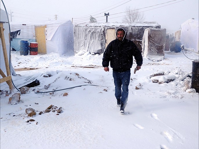 A man walks with a hammer after fixing plastic covers on tents in the snow-covered makeshift refugee camp of Terbol near the Bekaa Valley town of Zahleh in eastern Lebanon on December 11, 2013. Lebanese authorities are mobilising to help Syrian refugees living in makeshift camps during winter, as storm "Alexa" brings several days of rain, snow and a steep drop in
