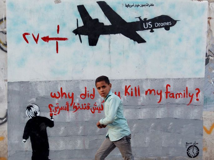 MH013 - Sanaa, -, YEMEN : A Yemeni boy (C) walks past a mural depicting a US drone and reading " Why did you kill my family" on December 13, 2013 in the capital Sanaa. A drone strike on a wedding convoy in Yemen killed 17 people, mostly civilians, medical and security sources said, adding grist to mounting criticism of the US drone war. AFP PHOTO/ MOHAMMED HUWAIS
