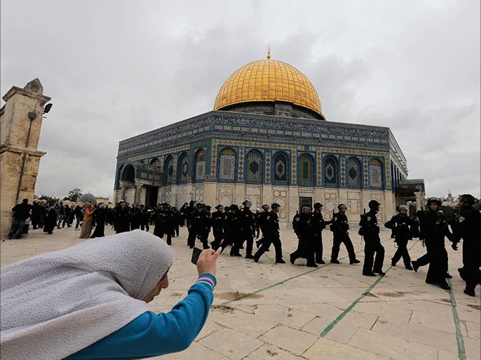 A Palestinian woman takes a picture as Israeli police walk in front of the Dome of the Rock during clashes with stone-throwing protesters after Friday prayers, outside al-Aqsa mosque in the compound known to Muslims as Noble Sanctuary and to Jews as Temple Mount, in Jerusalem's Old City December 6, 2013. Israeli police hurled stun grenades to disperse