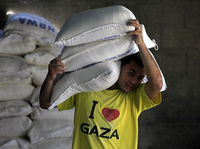 epa03690782 A Palestinian man carries sacks of food aid at the United Nations Relief and Works Agency (UNRWA) center in Al Shatea refugee camp in the west of Gaza City, 07 May 2013. EPA/MOHAMMED SABER