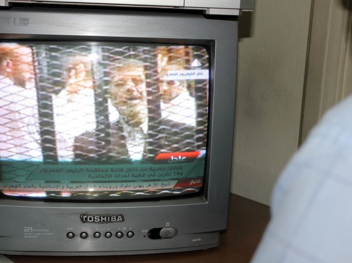 epa03935665 A man watches Egyptian television showing ousted president Mohamed Morsi standing behind bars during first trial session, in Cairo, Egypt, 04 November 2013. An Egyptian judge has adjourned the trial of Morsi until 08 January 2014. Morsi arrived on 04 November at the venue for his trial on charges of inciting the killing of opposition protesters, where he insisted that he is still the legitimate president. The so-called 'four-finger salute' has come to symbolize the lives lost during the dispersal of the Rabaa al-Adawiya protest camp by the Egyptian army. EPA/AMEL PAIN