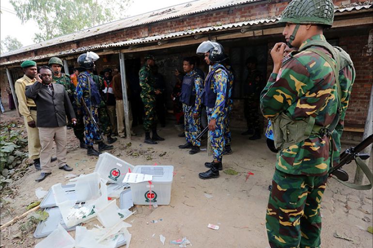 Bangladeshi police and soldiers stand next to damaged ballot boxes in front of a polling station after it was attacked by protestors in the northern town of Bogra on January 5, 2014. Protestors firebombed polling stations and attacked police as Bangladesh went ahead with a violence-plagued election boycotted by the opposition. AFP PHOTO/STR