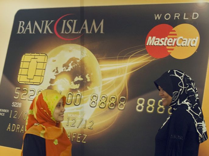 epa01953073 Malaysian Muslim women chat near a mock Islamic Bank Mastercard card during its launching in Kuala Lumpur, Malaysia, 03 December 2009. Malaysian Islamic Bank launches Asia Pacific's first Islamic world mastercard with Islamic syariah law based financial services. EPA/AHMAD YUSNI