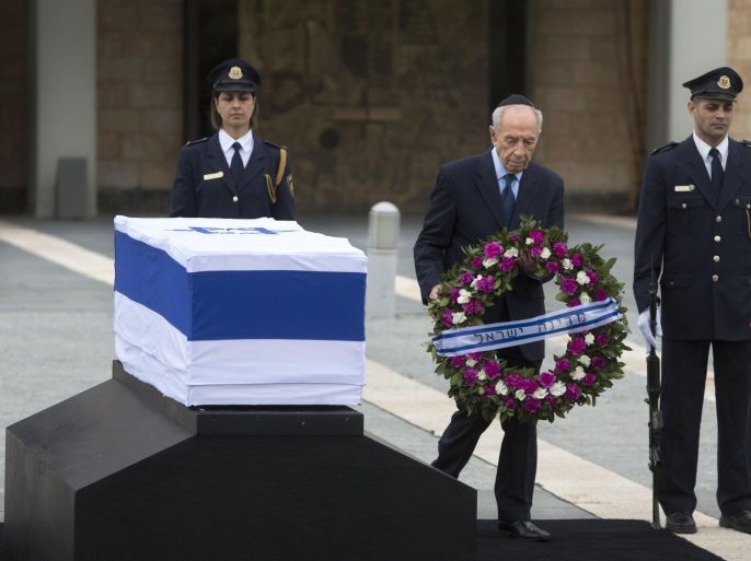 Israel's President Shimon Peres lays a wreath next to the coffin of late Israeli Prime Minister Ariel Sharon at the Knesset plaza, Israel's Parliament, in Jerusalem, Sunday, Jan. 12, 2014. Sharon, the hard-charging Israeli general and prime minister who was admired and hated for his battlefield exploits and ambitions to reshape the Middle East, died Saturday, eight years after a stroke left him in a coma from which he never awoke. He was 85. Hebrew on wreath reads: "The State of Israel." (AP Photo/Sebastian Scheiner)