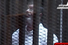 In this image taken from Egypt State TV, Egypt's toppled President Mohammed Morsi stands inside a glass-encased metal cage in a courtroom in Cairo, Egypt, Tuesday, Jan. 28. 2014. Morsi was, separated from other defendants for the start of a new trial Tuesday over charges from prison breaks during the country's 2011 revolution, state television reported. (AP Photo/Egyptian State TV)