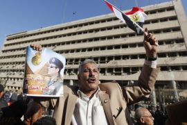 A supporter of Egypt's army chief General Abdel Fattah al-Sisi holds a poster of Sisi in front of the damaged Cairo Security Directorate building, which includes police and state security, after a bomb attack in downtown Cairo, January 24, 2014. A suicide bomber in a car blew himself up in the parking lot of a top security compound in central Cairo on Friday, killing at least four people in one of the most high-profile attacks on the state in months, security sources said. The poster reads "We will die and Egypt will live." REUTERS/Mohamed Abd El Ghany (EGYPT - Tags: POLITICS CIVIL UNREST CRIME LAW)