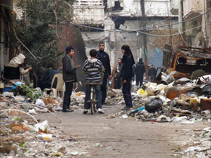 Civilians stand along a street amid garbage and rubble of damaged buildings in the besieged area of Homs January 27, 2014. The United States called on the Syrian government on Monday to allow aid convoys into the Old City of Homs, where "people are starving", and said that all civilians must be allowed to leave the besieged area freely. The evacuation of women and children fro