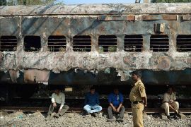 Indian railway officials sit beneath a burnt carriage of a long distance passenger train near Dahanu railway station, on the outskirts of Mumbai on January 8, 2014. A fire on an overnight train killed at least