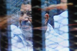 Egypt's ousted President Mohammed Morsi in a soundproof barred glass cage is seen on a monitor set up outside a courtroom where Morsi and 35 others are facing charges of conspiring with foreign groups and undermining national security, in Cairo, Egypt, Sunday, Feb. 16, 2014. Lawyers for Egypt's ousted president and his co-defendants walked out of court on Sunday to protest the soundproof glass cage in which defendants are held during proceedings, state TV reported. The cage was introduced after Morsi and his co-defendants interrupted the proceedings of other court cases by talking over the judge and chanting slogans. (AP Photo/Mohammed al-Law)